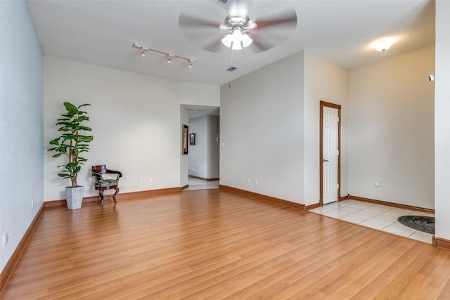 spare room with light wood-type flooring, a ceiling fan, visible vents, baseboards, and a textured ceiling