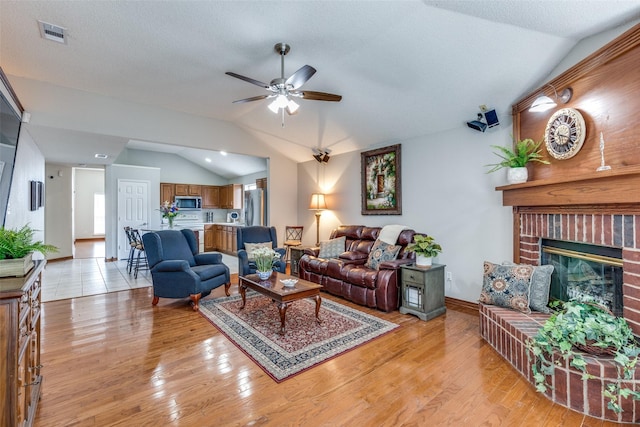 living room featuring visible vents, ceiling fan, a fireplace, light wood-type flooring, and lofted ceiling