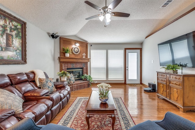 living area with a fireplace, ceiling fan, visible vents, a textured ceiling, and lofted ceiling