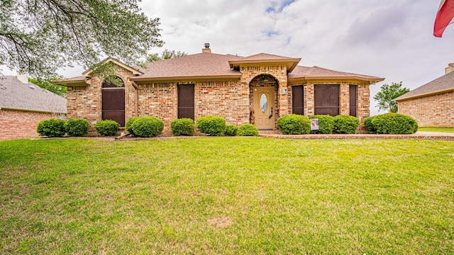 ranch-style home with a chimney, a front yard, a shingled roof, and brick siding