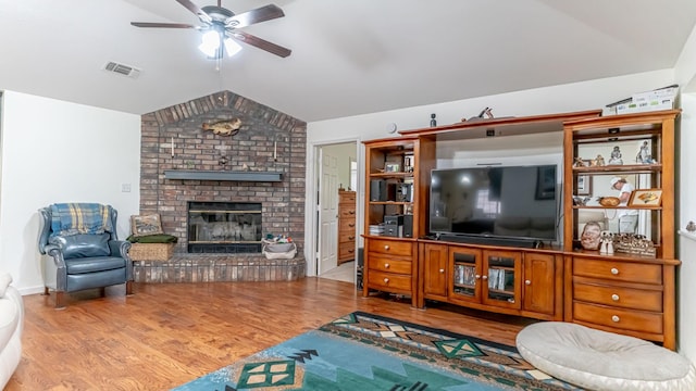 living area featuring wood finished floors, vaulted ceiling, ceiling fan, a brick fireplace, and visible vents