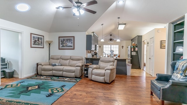 living room with light wood finished floors, a ceiling fan, vaulted ceiling, and baseboards