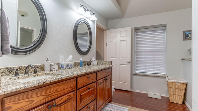 bathroom with baseboards, wood finished floors, double vanity, and a sink
