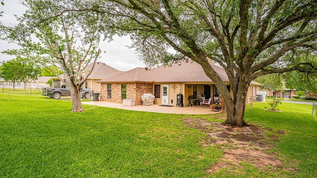 rear view of house with fence, roof with shingles, a patio area, and a yard