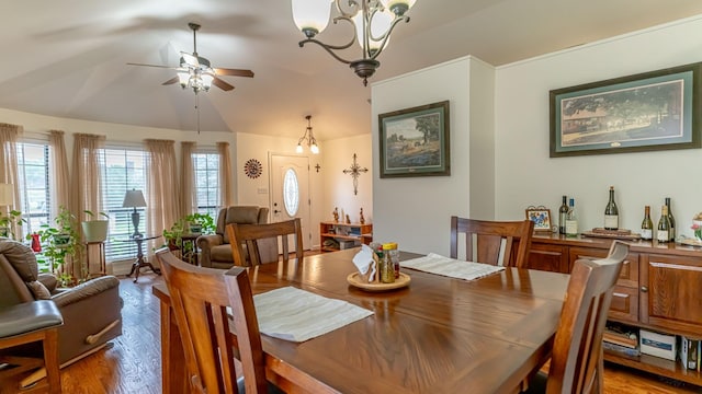 dining space with wood finished floors, ceiling fan with notable chandelier, and vaulted ceiling