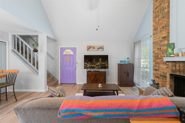 living room featuring stairs, light wood-style floors, a fireplace, baseboards, and high vaulted ceiling