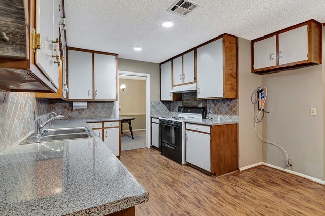 kitchen featuring visible vents, gas stove, under cabinet range hood, a sink, and light wood-type flooring