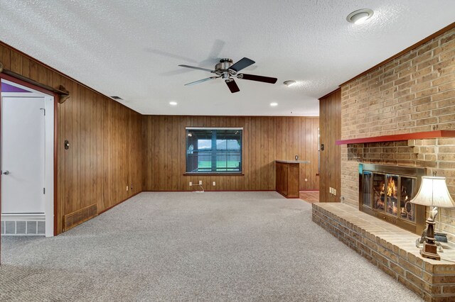 unfurnished living room featuring carpet, wooden walls, a ceiling fan, and a brick fireplace