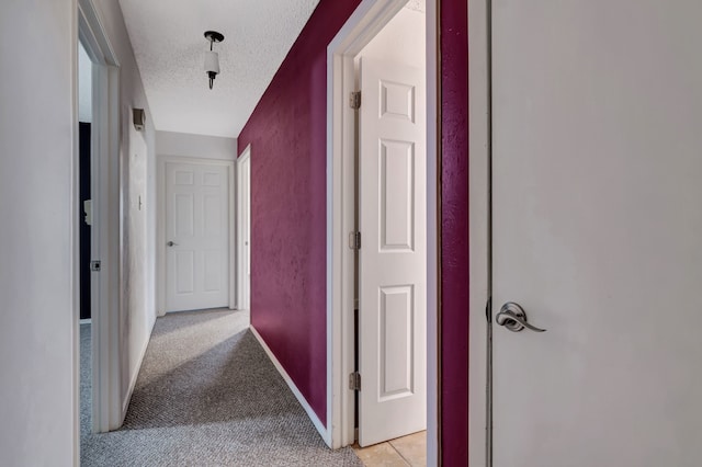 corridor with baseboards, a textured ceiling, and light colored carpet