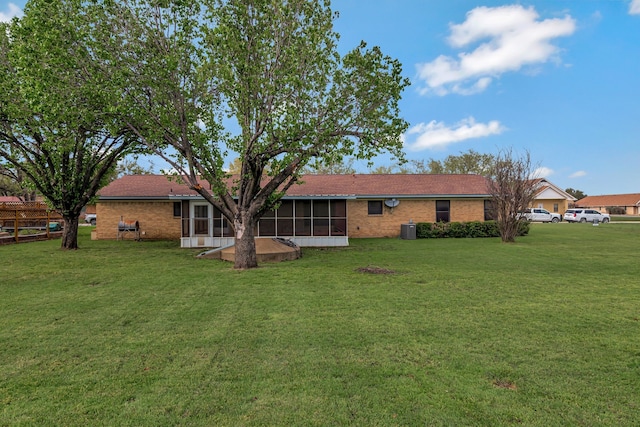 rear view of property featuring a yard, central AC unit, and a sunroom