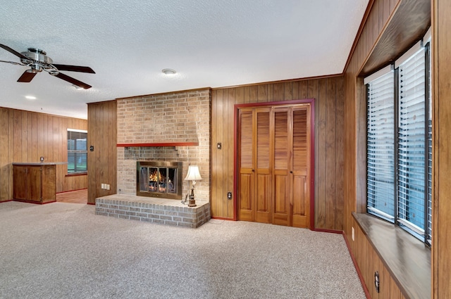 unfurnished living room with a brick fireplace, a textured ceiling, ceiling fan, and wood walls