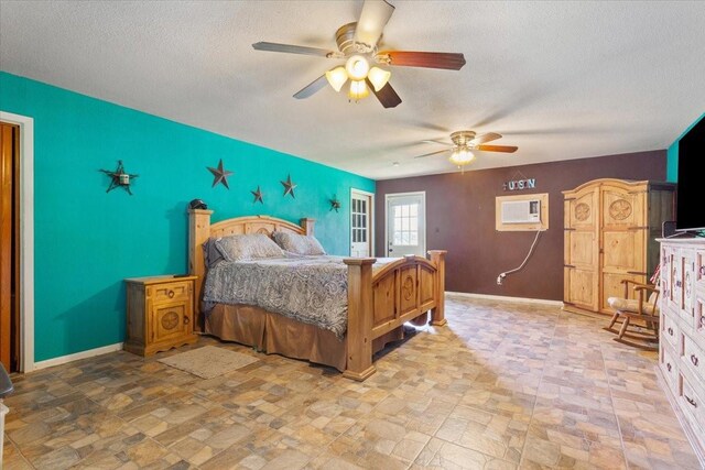 bedroom with a wall mounted AC, stone finish floor, baseboards, a textured ceiling, and an accent wall