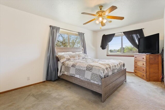 bedroom featuring light colored carpet, ceiling fan, baseboards, and multiple windows
