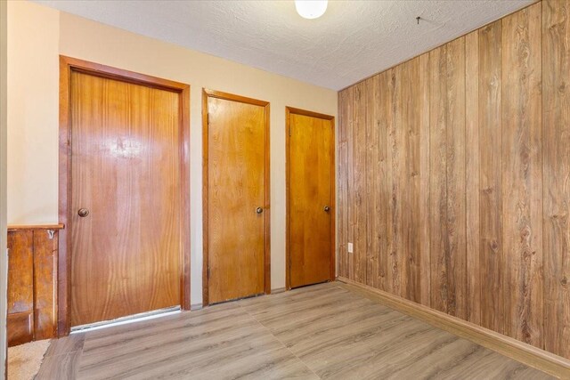 unfurnished bedroom with wood finished floors, wood walls, multiple closets, and a textured ceiling