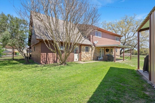 rear view of property with a yard, stone siding, and fence