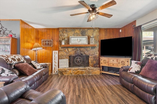 living room with wood walls, wood finished floors, a ceiling fan, and a stone fireplace