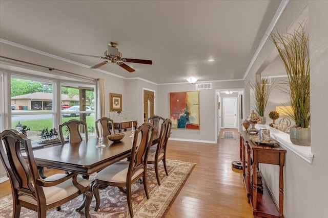 dining area with light wood-style floors, ornamental molding, baseboards, visible vents, and a ceiling fan