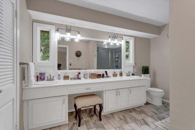 full bathroom with a stall shower, toilet, double vanity, and a sink