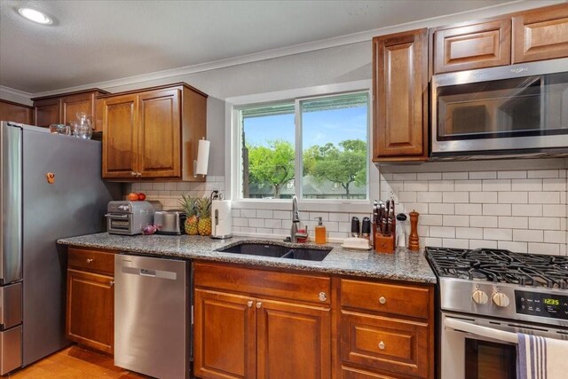 kitchen featuring brown cabinets, a sink, appliances with stainless steel finishes, stone countertops, and ornamental molding