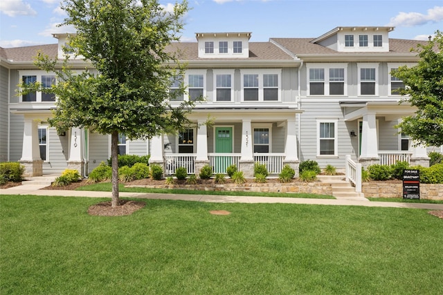 view of property with covered porch, a shingled roof, and a front lawn