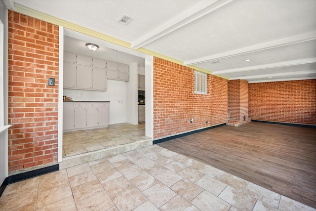 5816 Sandra Dr, Fort Worth, TX 76133 - unfurnished living room featuring beam ceiling, brick wall, baseboards, stone finish flooring, and visible vents