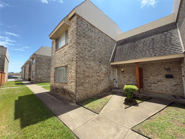 view of side of home with brick siding, a shingled roof, and a lawn
