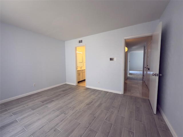 unfurnished bedroom featuring baseboards, visible vents, wood finished floors, and connected bathroom