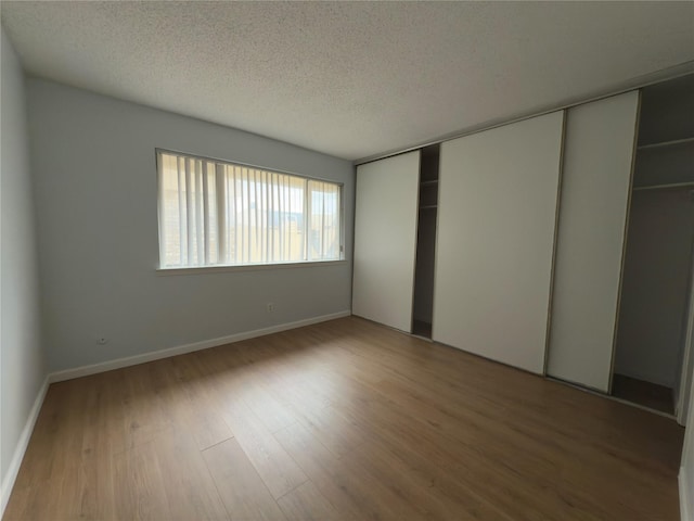 unfurnished bedroom featuring a textured ceiling, wood finished floors, baseboards, and a closet