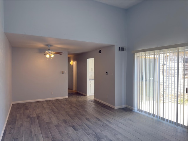 empty room with baseboards, visible vents, a ceiling fan, and dark wood-type flooring