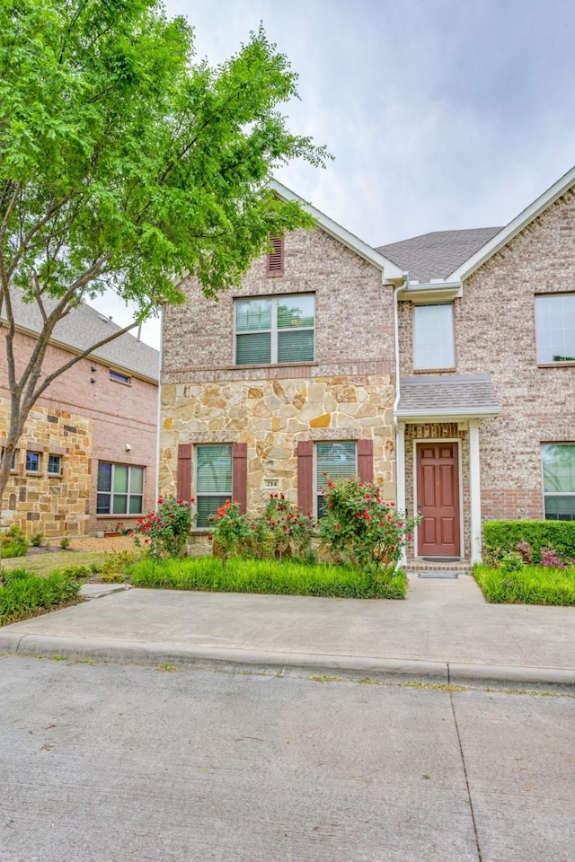 multi unit property featuring a shingled roof, brick siding, and stone siding