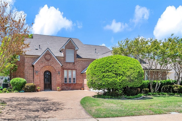 tudor-style house with brick siding, a shingled roof, and concrete driveway