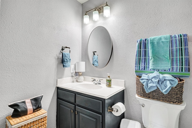 bathroom featuring toilet, a textured wall, and vanity