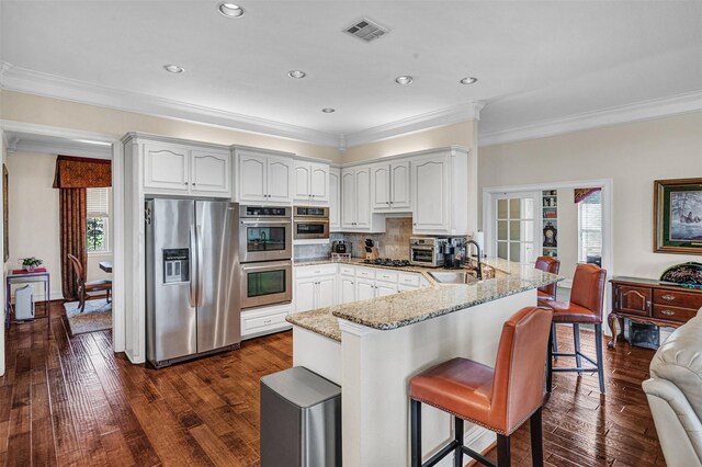 kitchen featuring visible vents, a peninsula, light stone countertops, a sink, and appliances with stainless steel finishes