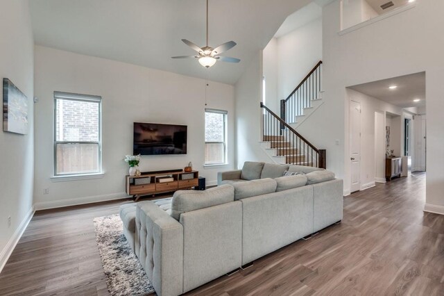 living room featuring stairway, ceiling fan, baseboards, wood finished floors, and high vaulted ceiling