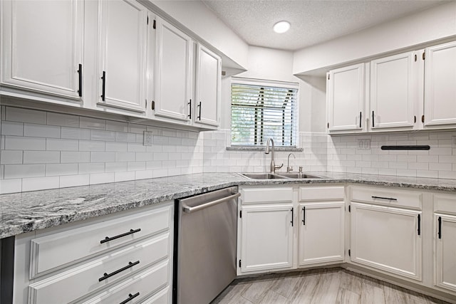 kitchen with a textured ceiling, white cabinetry, stainless steel dishwasher, and a sink