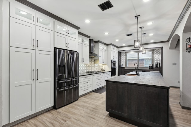 kitchen with visible vents, ornamental molding, wall chimney exhaust hood, a sink, and appliances with stainless steel finishes
