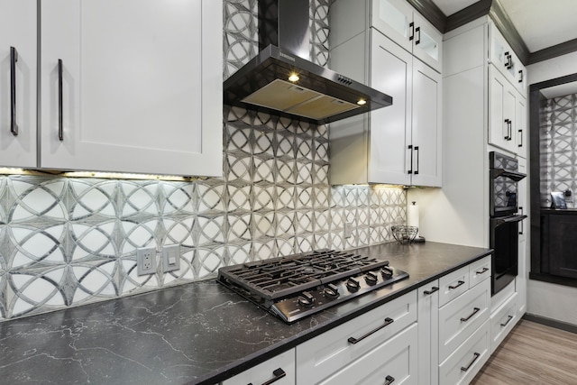 kitchen featuring wall chimney range hood, gas cooktop, white cabinets, and backsplash