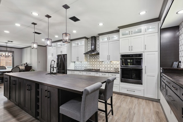 kitchen with backsplash, appliances with stainless steel finishes, a sink, wood counters, and wall chimney exhaust hood