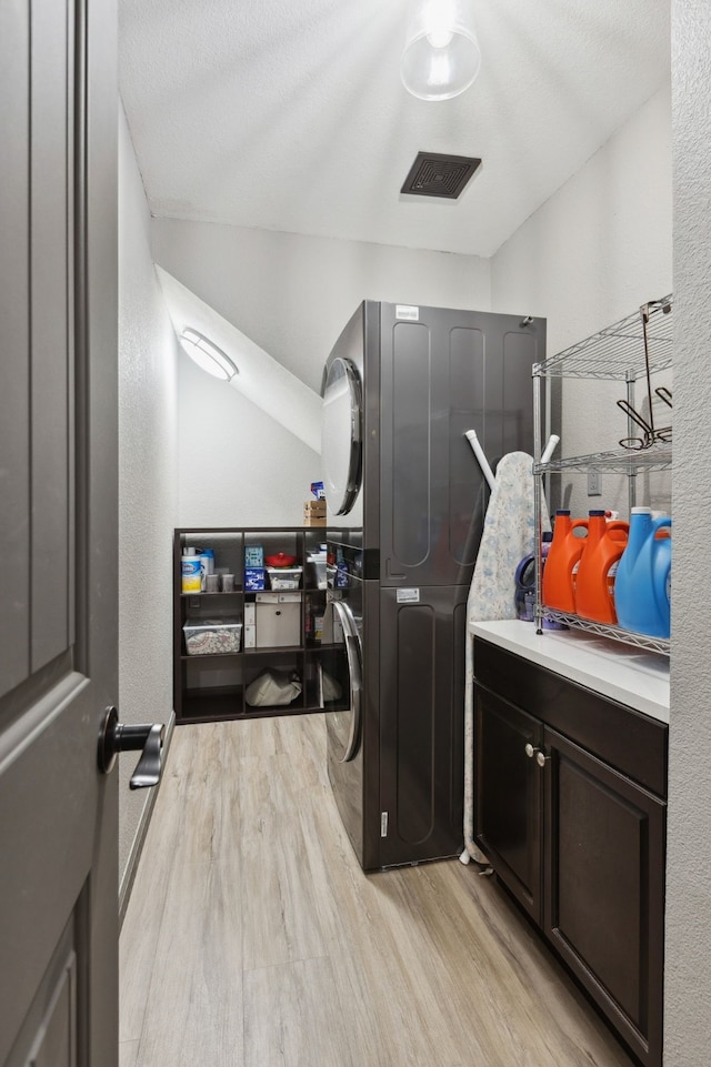 washroom with light wood-style floors, stacked washer and dryer, cabinet space, and visible vents