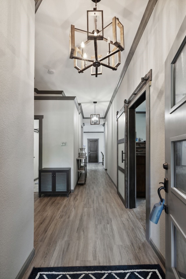 corridor with an inviting chandelier, ornamental molding, a barn door, and wood finished floors