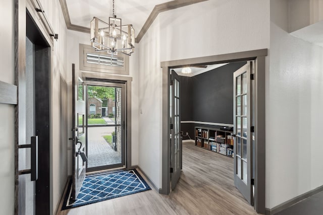 foyer entrance featuring baseboards, crown molding, wood finished floors, and a chandelier