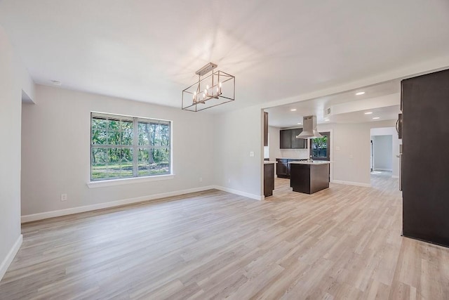 unfurnished living room with recessed lighting, a notable chandelier, light wood-style flooring, and baseboards