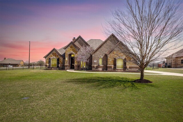 french country home featuring a front lawn, a chimney, stone siding, and fence