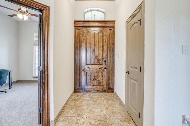 entryway with ceiling fan, plenty of natural light, light carpet, and baseboards