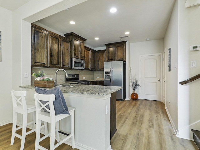 kitchen with light stone countertops, dark brown cabinets, light wood-style floors, and appliances with stainless steel finishes