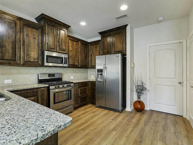 kitchen with dark brown cabinetry, light stone counters, appliances with stainless steel finishes, light wood finished floors, and visible vents