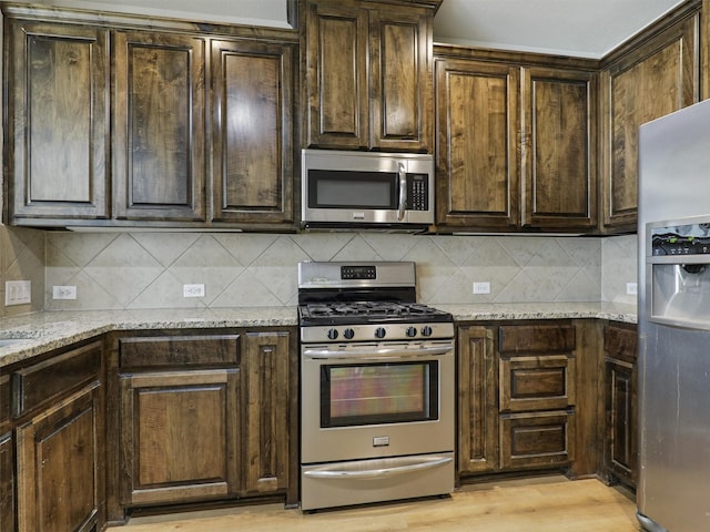 kitchen with tasteful backsplash, dark brown cabinetry, stainless steel appliances, and light stone counters