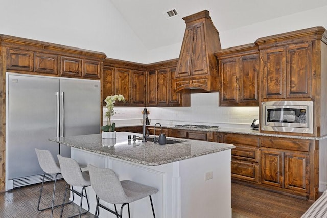 kitchen with light stone countertops, appliances with stainless steel finishes, vaulted ceiling, backsplash, and dark wood-style flooring