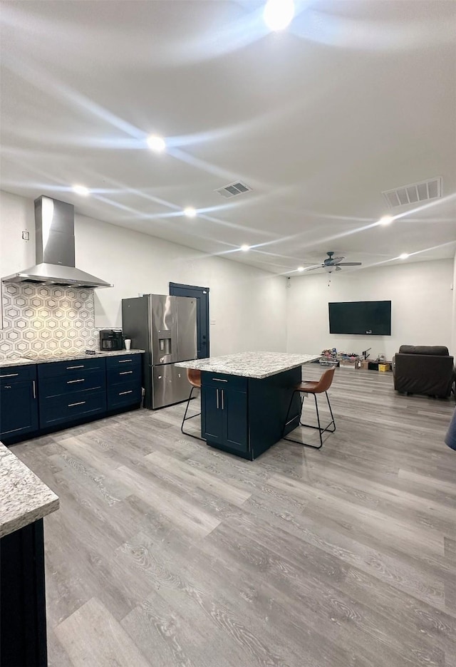 kitchen with a breakfast bar, visible vents, stainless steel fridge with ice dispenser, and wall chimney range hood