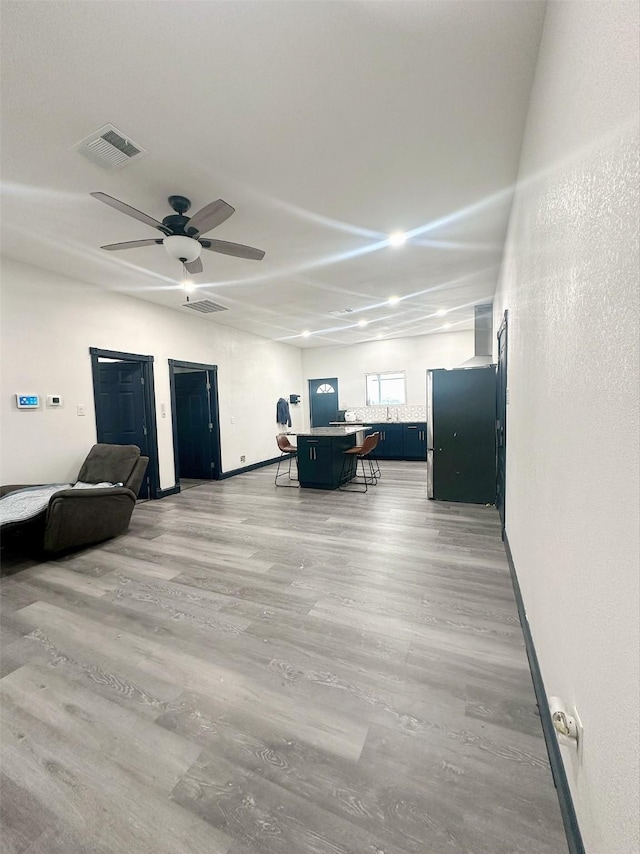 living area with light wood-type flooring, a ceiling fan, visible vents, and baseboards